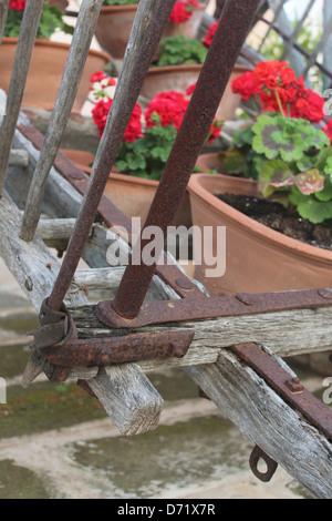 Nahaufnahme von rostigen Gelenk des alten Holzkarren mit roten Geranien in Terrakotta-Töpfe Stockfoto