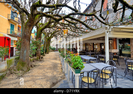 Outdoor-Restaurant mit Tischen und Stühlen unter Ästen in der Stadt von Sirmione, Italien. Stockfoto