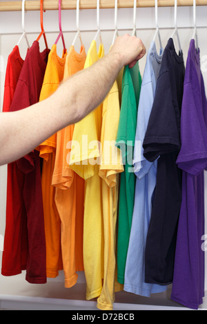 Männlich, Kommissionierung eine grüne Baumwoll-Shirt. Arm und Hand von einem weißen Mann gesehen, ein T-shirt aus einer Vielzahl von Hemden in einem Regenbogen von Farben in einem Schrank zu wählen. Stockfoto