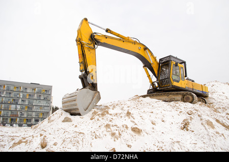 Bagger auf Steinbruch Sandkasten Haufen Boden bedeckt mit Schnee und neuen modernen Wohnhaus im Winter stehen. Bau Industrie w Stockfoto