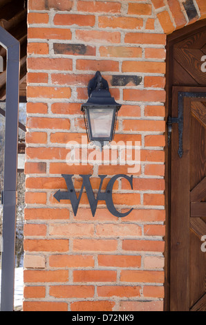 WC WC Symbol Zeichen auf roten Backsteinmauer in der Nähe von Retro-Beleuchtung Lampe. Stockfoto