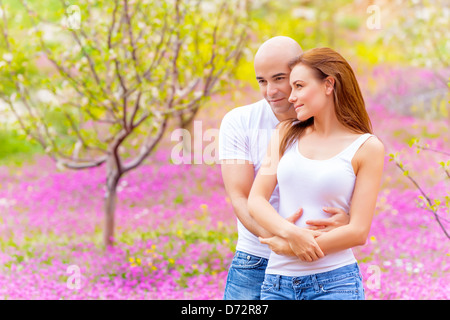 Umarmt im Freien im Frühling, Liebhaber verbringen Zeit auf Hinterhof, rosa Blumen Wiese genießen Familie, Konzept Stockfoto
