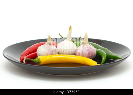 Drei Knoblauchzehen mit farbigen Chilischoten auf einem Teller Stockfoto