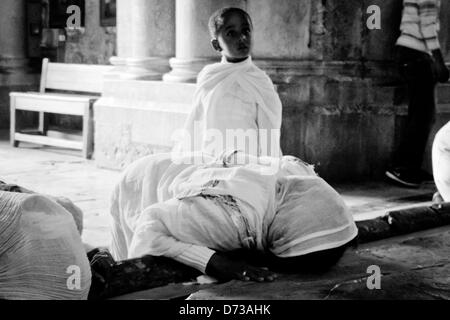 Ein kleiner Junge in zeremoniellen Roben blickt auf in Ehrfurcht, als seine Mutter bei der Salbung Stein am Eingang zur Kirche von der Grabeskirche kniet. Jerusalem, Israel. 28. April 2013.  Östliche orthodoxe Christen feiern am Palmsonntag, basierend auf dem Julianischen Kalender, an der Kirche der Grabeskirche. Stockfoto