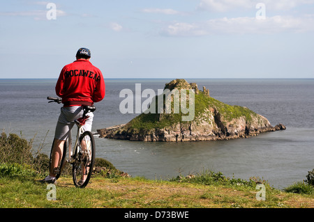 Mann in rot mit Blick auf Thatcher Rock, ein beliebter Ausflugsort in Torquay, Torbay, Devon, UK, Rocawear Mountainbike Stockfoto