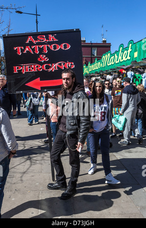 Porträt eines Mannes auf einer belebten Straße mit einem Schild Werbung einige Business, Camden, London, England, UK. Stockfoto