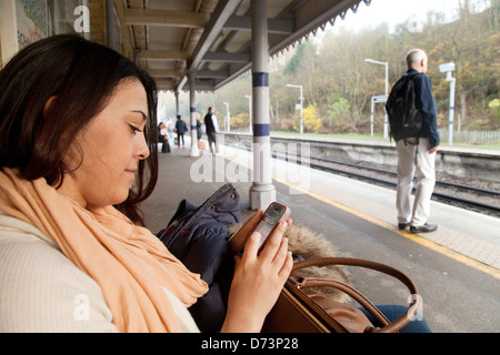 Eine junge Frau mit ihrem Mobiltelefon auf einem Bahnsteig warten auf einen Zug, London UK Stockfoto