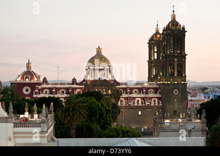 Seitenansicht mit goldenen Kuppel & Glocke Türmen Puebla Kathedrale gesehen über Bäume Zocalo in Dämmerung Glühen gegen rosa Himmel Mexiko Stockfoto