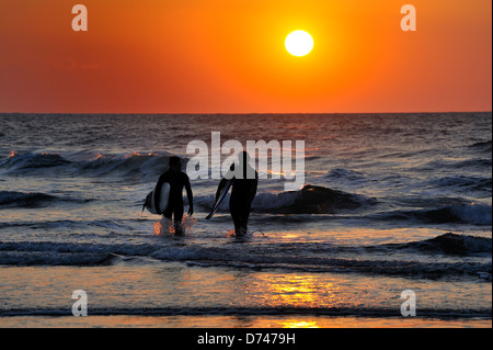 Die Sonne versinkt hinter zwei Surfer aus dem Meer nach ein Tag Surfen Stockfoto