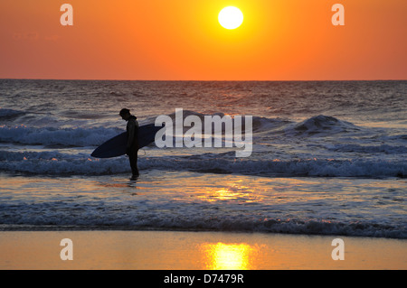 Die Sonne versinkt hinter ein Surfer, der aussieht wie er bessere Tage gehabt hat Stockfoto