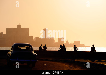 Skyline in La Habana, Cuba, bei Sonnenuntergang, mit Oldtimern auf der Straße und die Leute sitzen auf dem Malecon. Textfreiraum Stockfoto