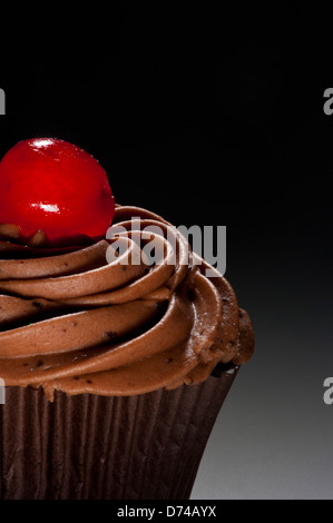 Schokoladen-Cupcake mit Schokoladenfrosting und Glacé-Kirsche auf schwarzem Hintergrund Stockfoto