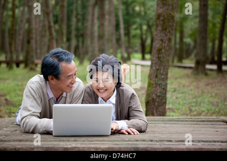 mittleren gealterten paar mit Laptop auf der Bank des Waldes liegend Stockfoto