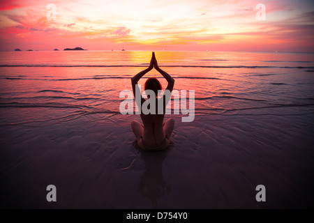 Junge Frau praktizieren Yoga am Strand bei Sonnenuntergang Stockfoto