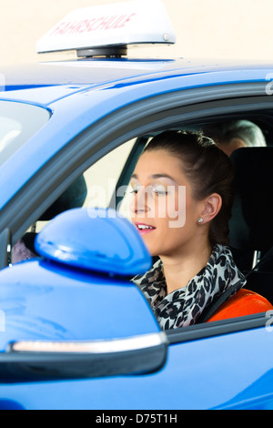 Fahrschule - junge Frau Steer sitzt eine Auto, vielleicht hat sie eine Fahrprüfung und der treibenden Prüfer auf den Rücksitzen Stockfoto