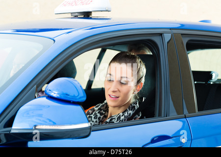 Fahrschule - junge Frau Steer sitzt eine Auto, vielleicht hat sie eine Fahrprüfung und der treibenden Prüfer auf den Rücksitzen Stockfoto