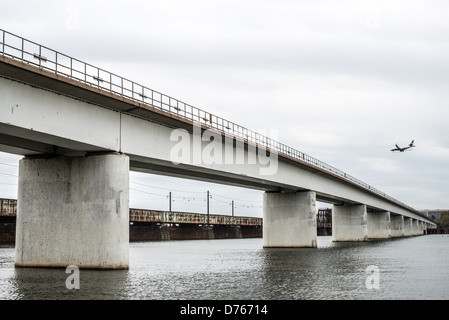 Intermodaler Güterzug Long Bridge Washington DC Frühling | WASHINGTON — Ein intermodaler Güterzug überquert die Long Bridge über dem Potomac River, während ein Jet auf den Ronald Reagan Washington National Airport sinkt, was den multimodalen Stau an dieser Potomac-Kreuzung in Washington, D.C. veranschaulicht. Die Stahl-Eisenbahnbrücke, die von einer hölzernen Vorgängerin aus dem Jahr 1809 neu gebaut wurde, verläuft neben den Betonhöhen des 14th-Street-Brückenkomplexes. Stockfoto