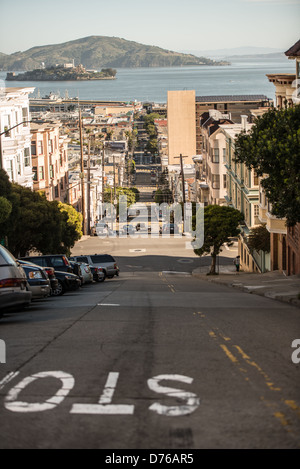 Taylor Street Steep Hill Alcatraz View San Francisco California // SAN FRANCISCO, Kalifornien – die Taylor Street führt steil hinunter durch San Franciscos Stadtviertel North Beach und bietet einen Blick auf Alcatraz Island und San Francisco Bay. Die Straße gehört zu den berühmten steilen Durchgangsstraßen der Stadt, die San Franciscos hügeliges Gelände prägen. North Beach liegt an der nördlichen Uferpromenade und ist weithin bekannt als das italienisch-amerikanische Viertel der Stadt und historisches Zentrum der Beat Generation Kultur. Alcatraz Island, sichtbar in der Entfernung über die Bucht, diente von 1934 bis 196 als Bundesgefängnis Stockfoto