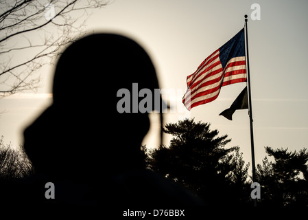 WASHINGTON, DC, Vereinigte Staaten – eine der Statuen von Soldaten am Korean war Veterans Memorial in der National Mall ist Washington DC, das sich vor der Sonne befindet und dahinter eine amerikanische Flagge im Wind weht. Stockfoto