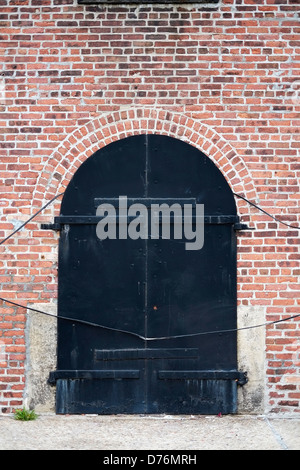 Große gewölbte schwarze Holztüren in einer roten Backsteinwand in Red Hook, Brooklyn, New York.k. Stockfoto