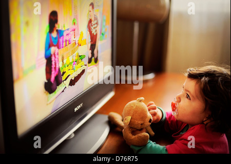 Kleinkind / Kind vor dem Fernseher mit Teddybär und Puppe Stockfoto