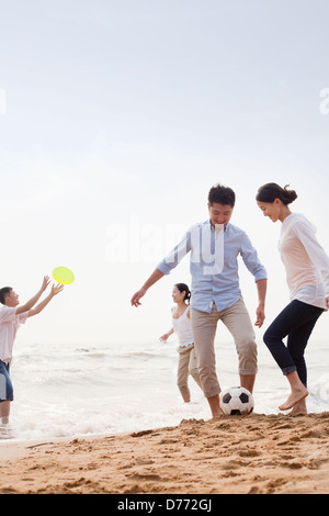 Vier junge Menschen spielen Fußball und Frisbee am Strand, China Stockfoto