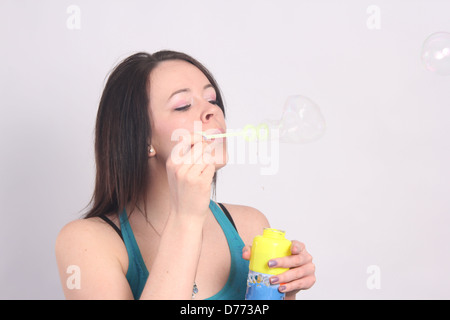 Sehr hübsche junge Frau bläst Seifenblasen durch einen kleinen Zauberstab. Stockfoto