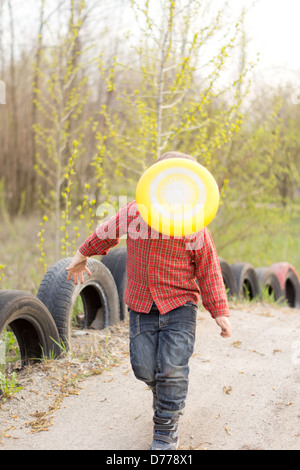 Kleiner Junge spielt auf einer Landstrasse mit einer Frisbee die fliegen durch die Luft, die sein Gesicht verdeckt ist Stockfoto
