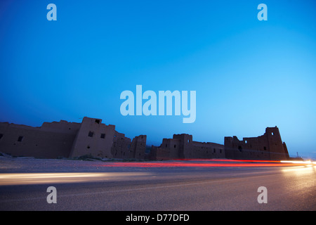 Ruinen von irdenen Wohnungen moderne Asphaltstraße helle Streifen vorbeifahrende Fahrzeuge Marokko Stockfoto