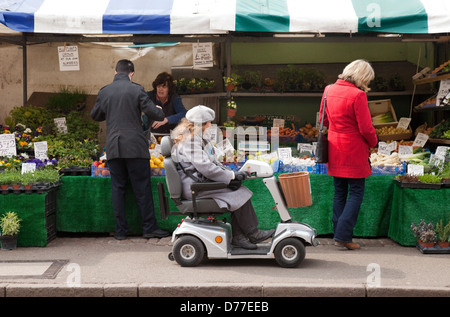 Eine behinderte Frau in einem Mobilität Buggy Einkaufen in einem Stall in Cambridge Markt, Cambridgeshire UK Stockfoto