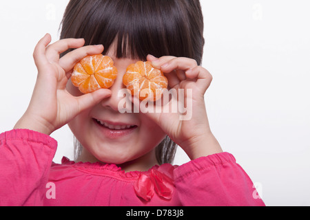 Kleines Mädchen hält Mandarinen vor ihren Augen Studio gedreht Stockfoto