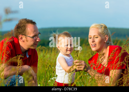 Eltern mit Kind in die Wiese und Löwenzahn Samen bei Sonnenschein weht Stockfoto