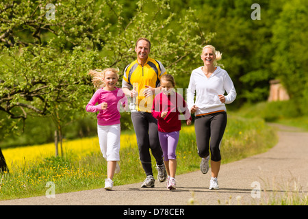 Glückliche Familie mit zwei Mädchen laufen oder Joggen für Sport und besserer Fitness auf einer Wiese im Sommer Stockfoto