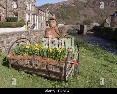 Afon Colwyn Fluss mit Narzissen in ungewöhnlichen Dreirad Blume Pflanzer am Ufer im Frühjahr. Beddgelert, Gwynedd, Nordwales, UK Stockfoto