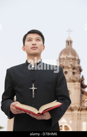 Junger Priester Blick in Himmel vor Kirche Stockfoto