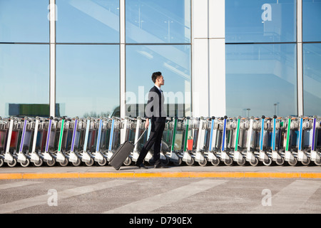 Reisende mit Koffer neben Zeile der Gepäckwagen am Flughafen Stockfoto