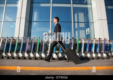 Reisende zu Fuß schnell neben Zeile der Gepäckwagen am Flughafen Stockfoto