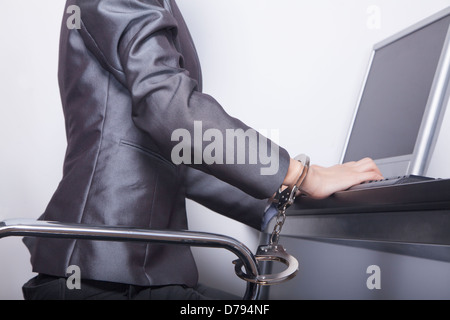 Junge Geschäftsfrau mit Handschellen gefesselt auf ihrem Bürostuhl Stockfoto