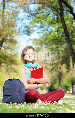 Studentin mit Notebook und Kopfhörer sitzen auf einer Wiese in einem park Stockfoto