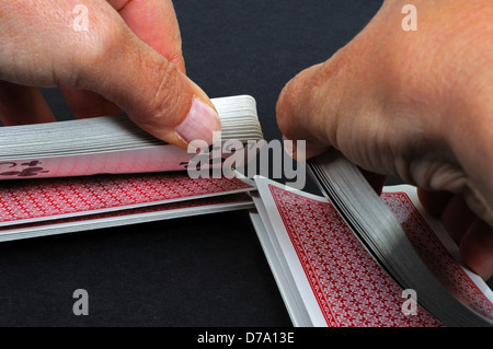 Frau, die ein Kartenspiel vor einem schlichten schwarzen Hintergrund mischt. Stockfoto
