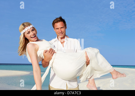 Bräutigam trägt Braut am schönen Strandhochzeit Stockfoto