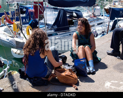 Zwei junge Frauen saßen in der Sonne auf dem Kai, Padstow, Cornwall, UK 2013 Stockfoto