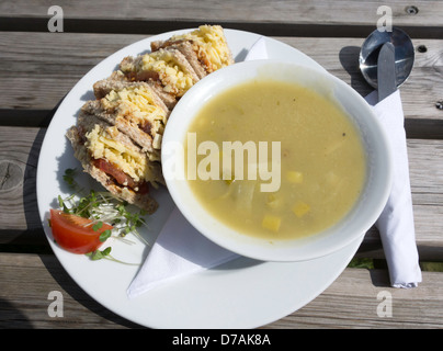 Café Mittagessen eine Schüssel mit Lauch und Kartoffel Suppe mit einem Cheddar-Käse und Gurke Sandwich draußen in der Sonne Stockfoto