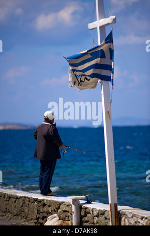 Ein Mann unter einer verwahrloster griechische Flagge in Mykonos Griechenland Angeln. Stockfoto