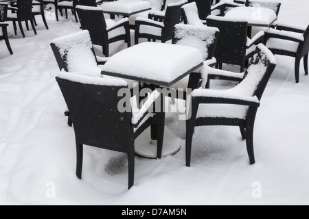 Stühle und Tische, die zu Beginn des Frühlings mit Schnee bedeckt Stockfoto