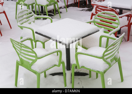 Stühle und Tische, die zu Beginn des Frühlings mit Schnee bedeckt Stockfoto