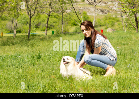 Ziemlich lässig junge Frau in Jeans bücken und spielt mit ihren niedlichen kleinen langhaarigen Hund im grünen Rasen auf dem Lande. Stockfoto