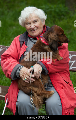 Eine ältere Frau mit einem Hund auf einer Bank, alte Frau Altern, ältere Frau Hund, Umarmung 70er Rentner auf einer Gartenbank ältere Frau Hund Stockfoto