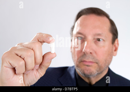 Älterer Erwachsene Mann Medizin Kapsel hält in seiner Hand mit ihm im Hintergrund unscharf und konzentriert sich auf die Kapsel. Stockfoto