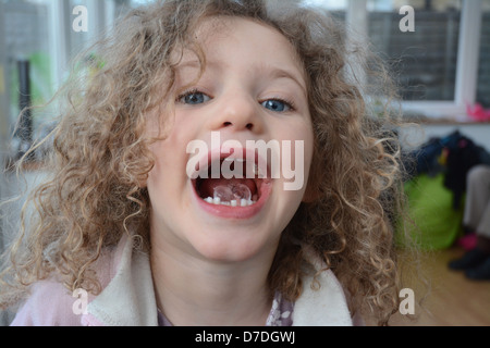 Fünf Jahre altes Mädchen mit lockigen Haaren und blauen Augen zeigen einen Eiswürfel in ihren offenen Mund Stockfoto